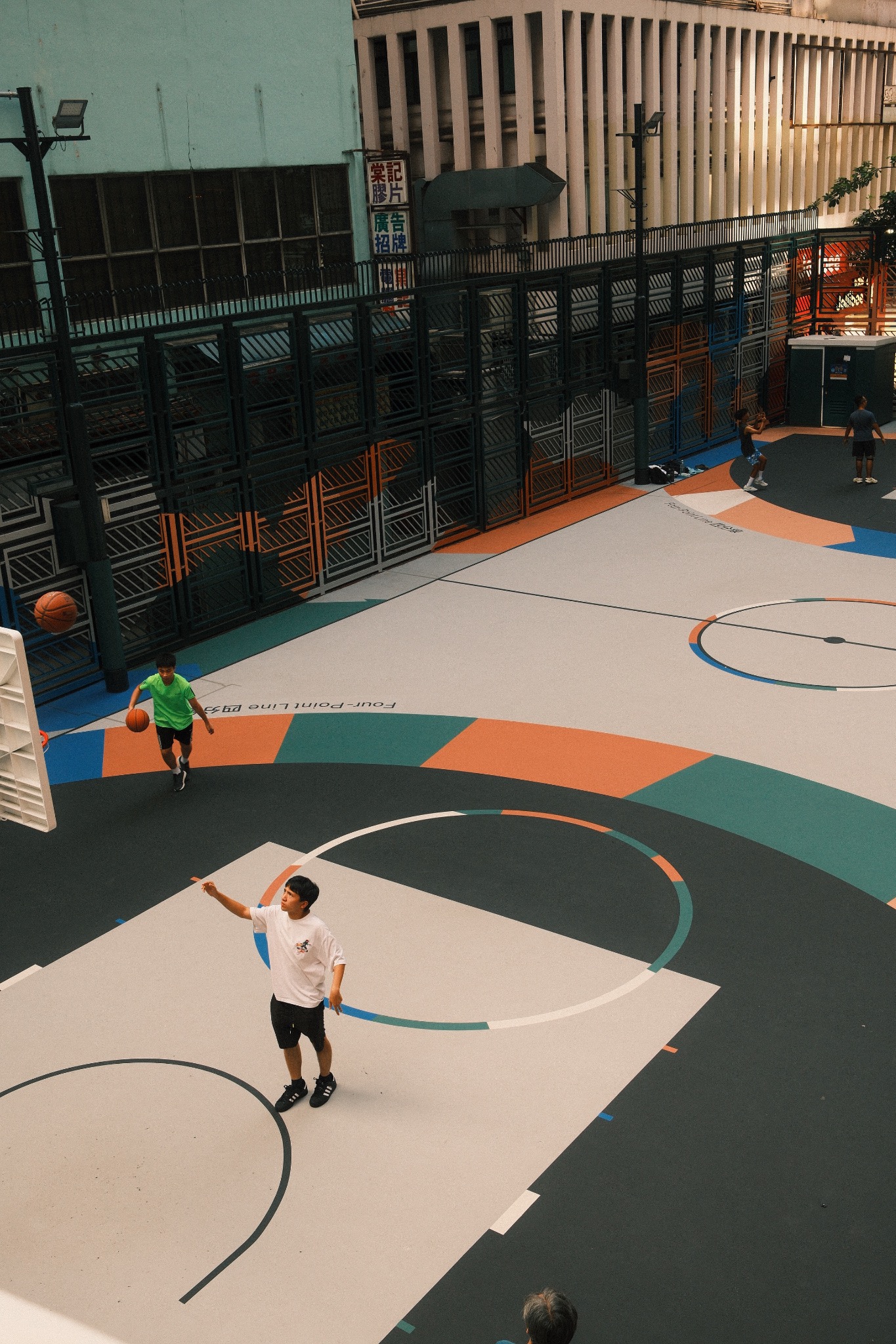Basketball players on a geometric teal, orange and cream court, surrounded by urban buildings.
